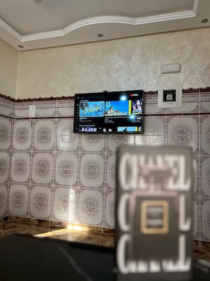 Ein Zimmer mit an der Wand befestigtem Fernseher, Wandpapier mit Muster und einer Tür mit Griff.