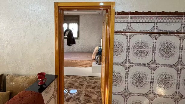 Ein Zimmer mit Wand aus gemusterten Fliesen, einem Holzrahmen an der Tür und einem Bett mit gemustertem Überwurf.