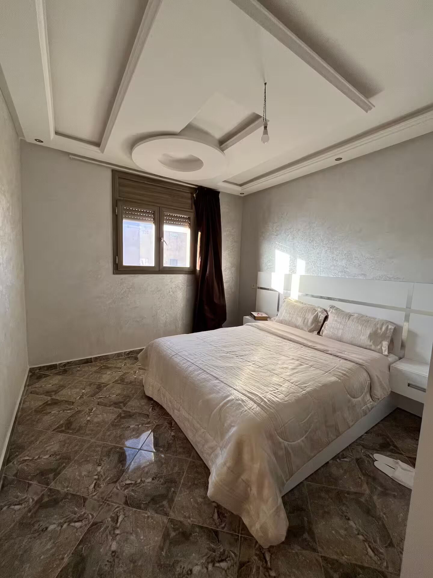 A bedroom with a large bed, a nightstand, a window with curtains, and a ceiling light fixture.