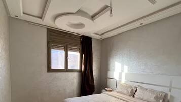 A bedroom with a large bed, a nightstand, a window with curtains, and a ceiling light fixture.