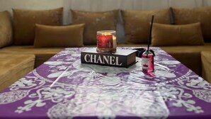 Ein Wohnzimmer mit einer Couch, einem Tisch mit dem Buch 'CHANEL', einer Kerze und einer Parfumflasche.