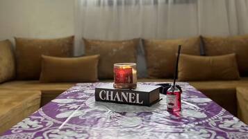Un salon avec un canapé, une table sur laquelle repose un livre intitulé « CHANEL », une bougie et un flacon de parfum.