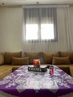 Ein Wohnzimmer mit einer Couch, einem Tisch mit dem Buch 'CHANEL', einer Kerze und einer Parfumflasche.