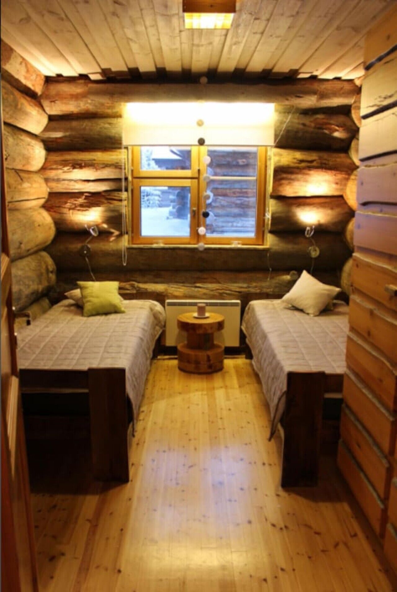 Ein Blockhauszimmer mit zwei Betten, einem Tisch in der Mitte und einem Fenster mit Aussicht.