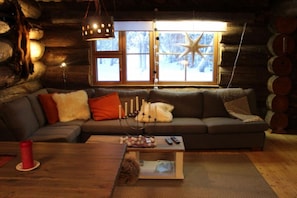 A cozy cabin interior with a sofa, a coffee table, and a window with a star decoration. - Ruka Chalet Roma | Traditional 2BR Log Apt | Sauna (Ruka)