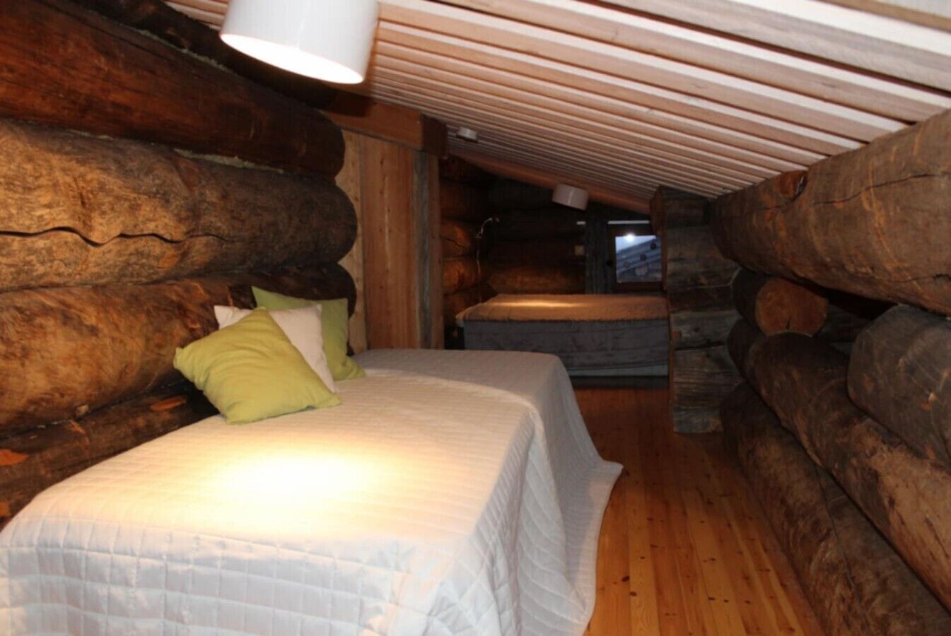 Une chambre dans un chalet en rondins, avec un lit, des oreillers et un plafond en bois.