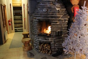 A stone fireplace with a fire, a white Christmas tree, and a log storage area. - Ruka Chalet Roma | Traditional 2BR Log Apt | Sauna (Ruka)