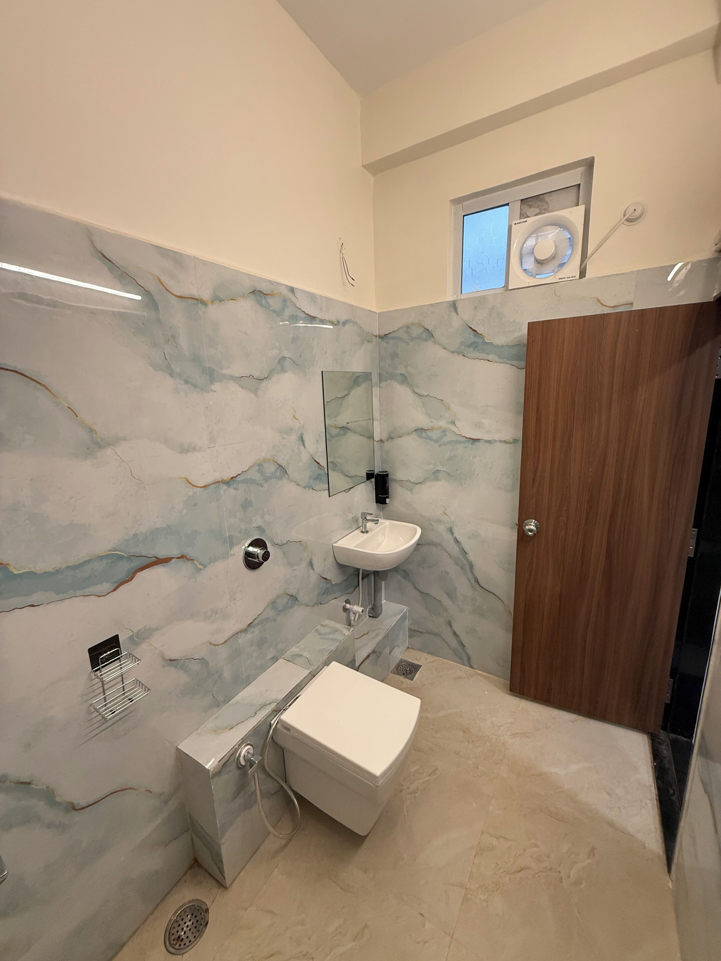A bathroom with a marble wall, a sink, a mirror, and a wooden door.
