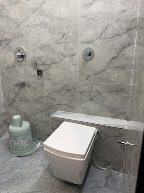 A bathroom with a toilet, a shower, and a marble wall.