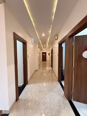 A hotel corridor with marble flooring, wooden doors, and recessed lighting.