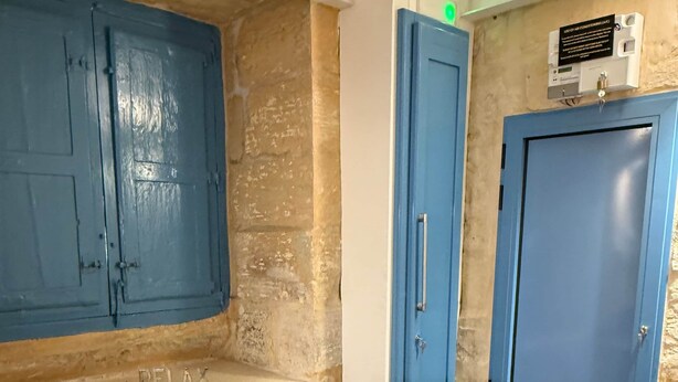 Una habitación con una mesa de madera, dos puertas azules, un aire acondicionado instalado en la pared y una planta pequeña sobre la mesa.