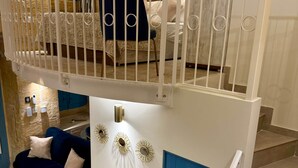 Un interior de varios niveles con una escalera, una puerta azul, una barandilla blanca y un sofá.