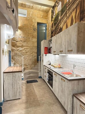 Una cocina moderna con paredes de piedra, horno empotrado y una escalera que sube a un nivel superior.