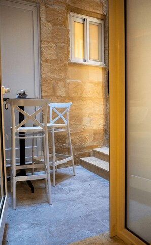 A narrow stairway leading to a door, with a white chair and a small table with a plant on the left. - Valletta City Suites Barrakka + Knight's Rest (Valletta)