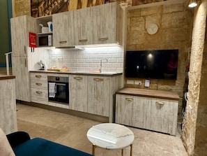 A compact kitchen with a microwave, oven, and a flat-screen TV mounted on the wall. - Valletta City Suites Barrakka + Knight's Rest (Valletta)