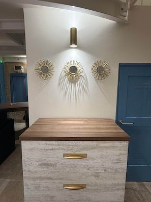 A room with a wooden cabinet, a wall-mounted light fixture, and three sunburst wall decorations. - Valletta City Suites Barrakka + Knight's Rest (Valletta)