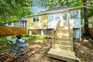 A residential property with a wooden deck, a brick patio, and a small outdoor seating area with a table and chairs. - Sunny, Updated Cottage in Hillcrest / Mid-Term Rental House (Little Rock)