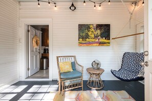A room with a wicker chair, a small round table, a hanging light fixture, and a painting on the wall. - Sunny, Updated Cottage in Hillcrest / Mid-Term Rental House (Little Rock)