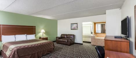 Habitación de hotel con cama, escritorio, silla, televisor y baño visible a través de una puerta abierta.