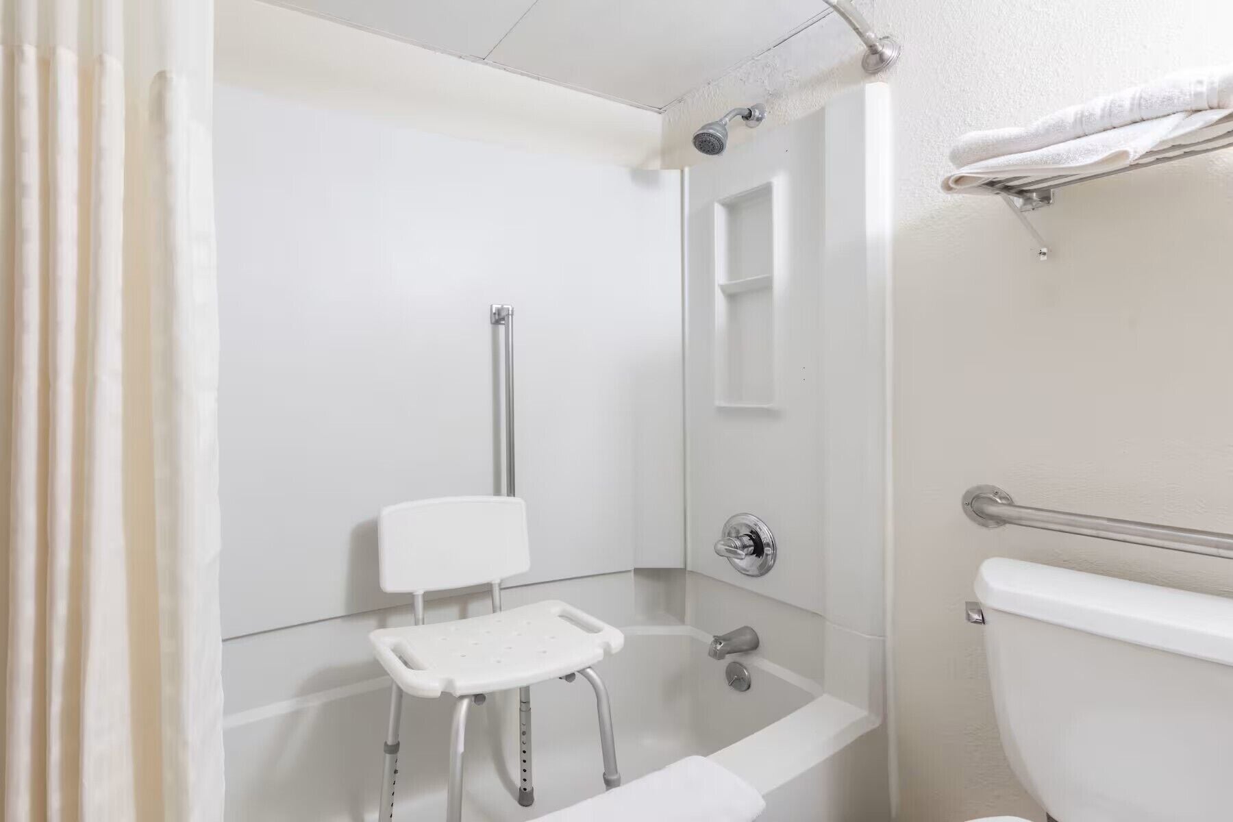A bathroom with a shower, toilet, and a small white bench.