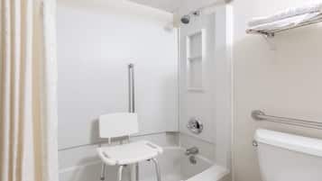 A bathroom with a shower, toilet, and a small white bench.