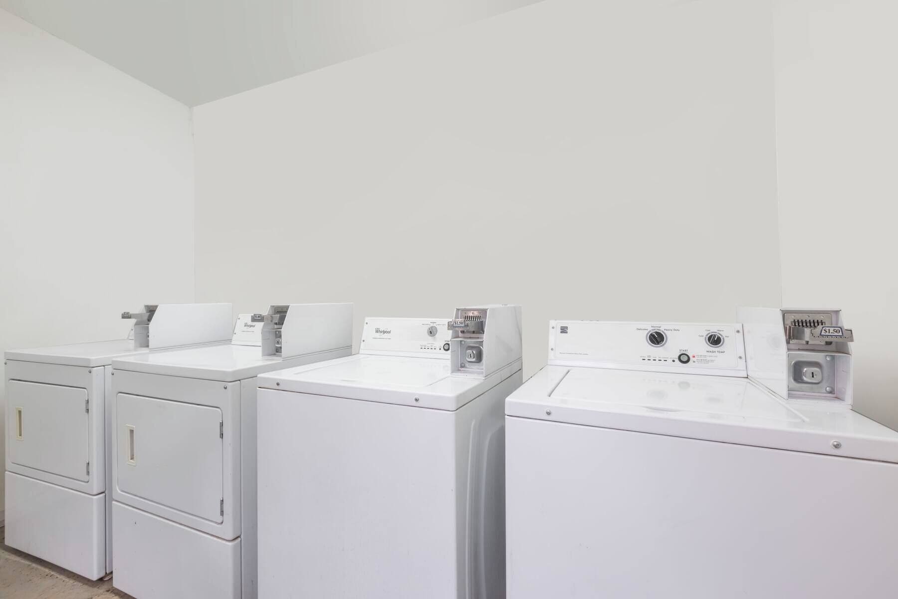 A laundry room with four white front-loading washers and dryers.