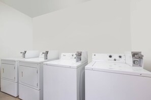 A laundry room with four white front-loading washers and dryers. - The Executive Inn & Suites Midland (Midland)