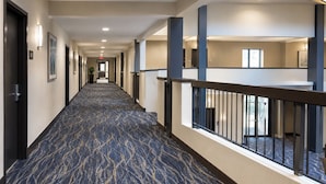 A hotel corridor with a patterned carpet, doors, and a railing overlooking a lower level. - The Executive Inn & Suites Midland (Midland)