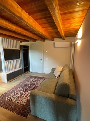 A living room with a sofa, a patterned rug, and wooden ceiling beams.