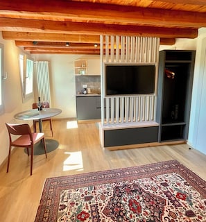 A modern living room with a wooden ceiling, a TV stand, a dining area with a table and chairs, and a patterned rug. - Private apartment in a beautiful house in Guia di Valdobbiadene with a view of the vineyards. (Veneto)