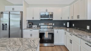 A modern kitchen with white cabinets, stainless steel appliances, and a granite countertop. - Shoreline Retreat - New Modern Luxury Waterfront Escape -Dock & Water Toys (Sterling)