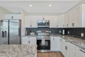 A modern kitchen with white cabinets, stainless steel appliances, and a granite countertop. - Shoreline Retreat - New Modern Luxury Waterfront Escape -Dock & Water Toys (Sterling)