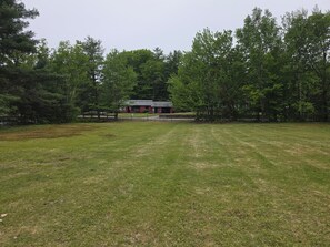 A grassy field with a building in the distance, surrounded by trees.
