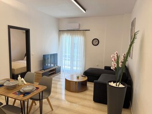 Ein modernes Wohnzimmer mit Flachbildfernseher, Esstisch gedeckt mit Tellern, einer Couch und einer Topf-Orchidee.