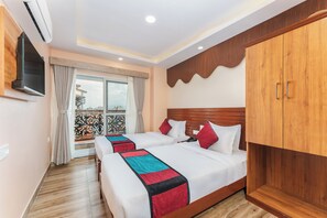 A hotel room with two beds, a wooden wardrobe, a TV mounted on the wall, and a balcony with a view of buildings. - Aarohan Hotel Thamel (Kathmandu)