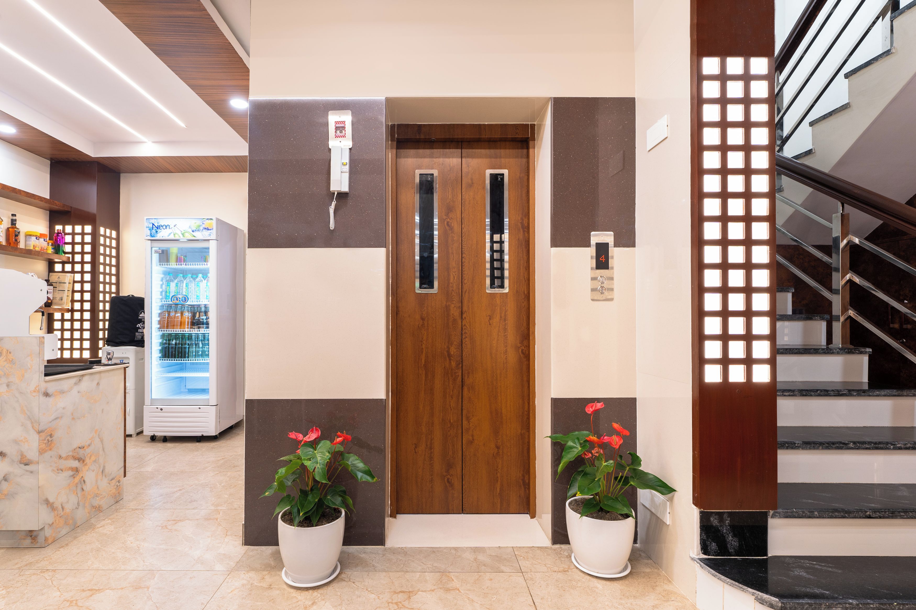 Un vestíbulo de hotel con una recepción, un refrigerador, una puerta de madera y una escalera.