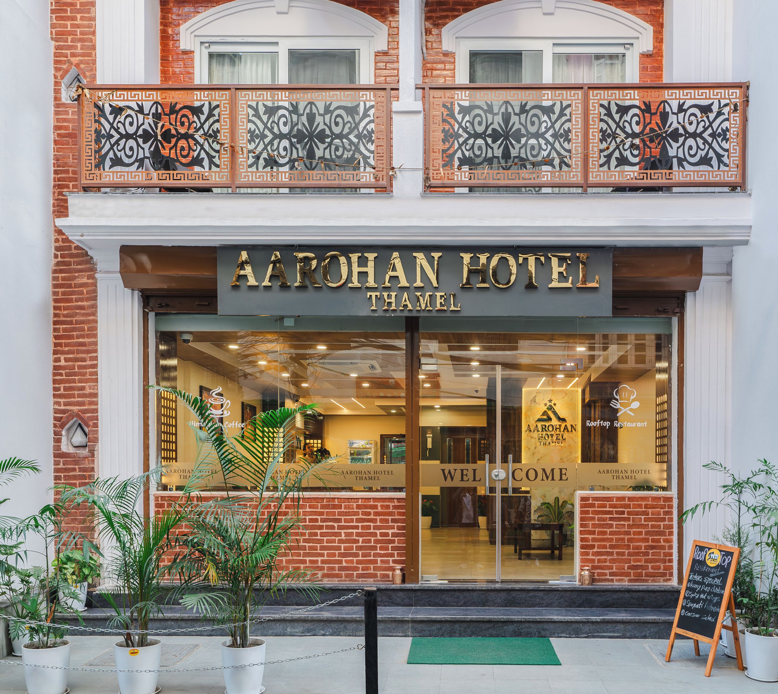 Exterior del HOTEL AAROHAN THAMEL, con una entrada despejada, un balcón con barandillas decorativas y un letrero para el Restaurante en la Azotea.