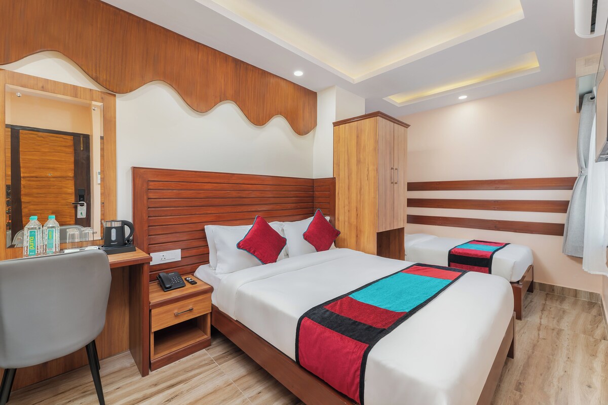 A hotel room with a large bed, a bedside table with a phone and water bottles, a wooden wardrobe, and a mirror.