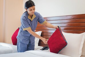 A person arranging a red throw pillow on a bed with white bedding and a wooden headboard. - Aarohan Hotel Thamel (Kathmandu)