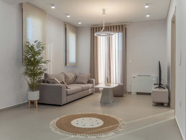A modern living room with a sofa, a small table, a potted plant, and a television. - καινούριο άνετο διαμέρισμα με μπαλκόνια και πάρκινγκ. Πλήρες εξοπλισμένο (CHIOS)
