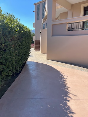 Ein gepflasterter Weg führt zu einem Gebäude mit Treppe und einer Hecke.