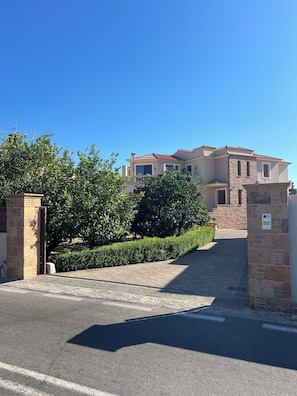 A residential property with a paved driveway leading to a gated entrance, surrounded by greenery and stone walls. - καινούριο άνετο διαμέρισμα με μπαλκόνια και πάρκινγκ. Πλήρες εξοπλισμένο (CHIOS)