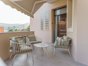 Ein Balkon mit zwei weißen Korbstühlen, einem kleinen runden Tisch, einer Holztür und Blick aufs Meer.