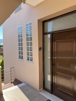 A building with a large brown door, a small window, and a metal railing. - καινούριο άνετο διαμέρισμα με μπαλκόνια και πάρκινγκ. Πλήρες εξοπλισμένο (CHIOS)