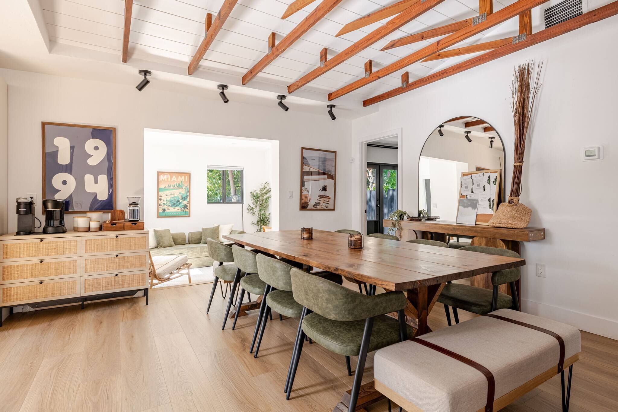 A modern dining area with a wooden table, cushioned chairs, and a high ceiling with exposed beams.