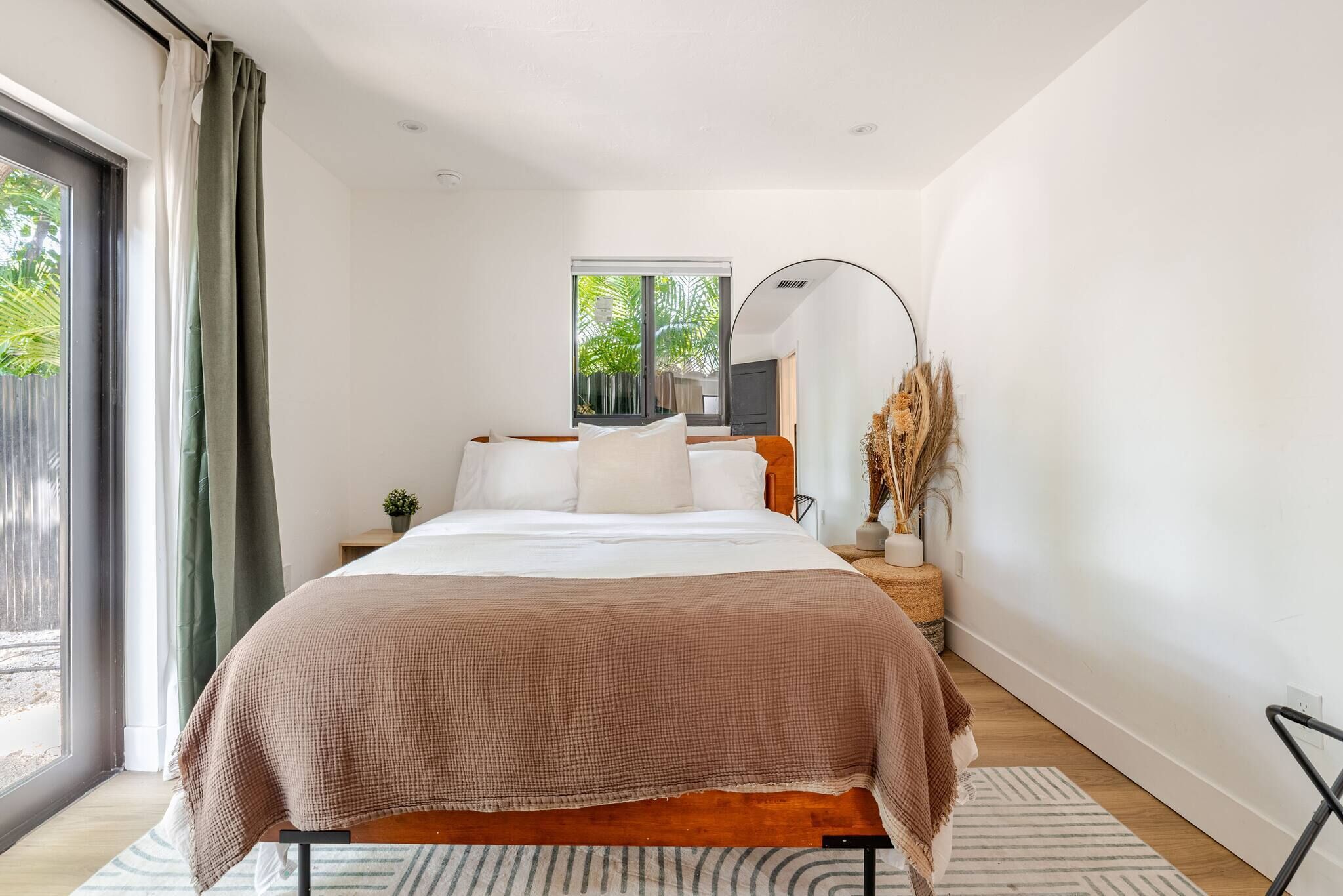 A bedroom with a bed, a window, a bedside table, a lamp, and a view of greenery outside.