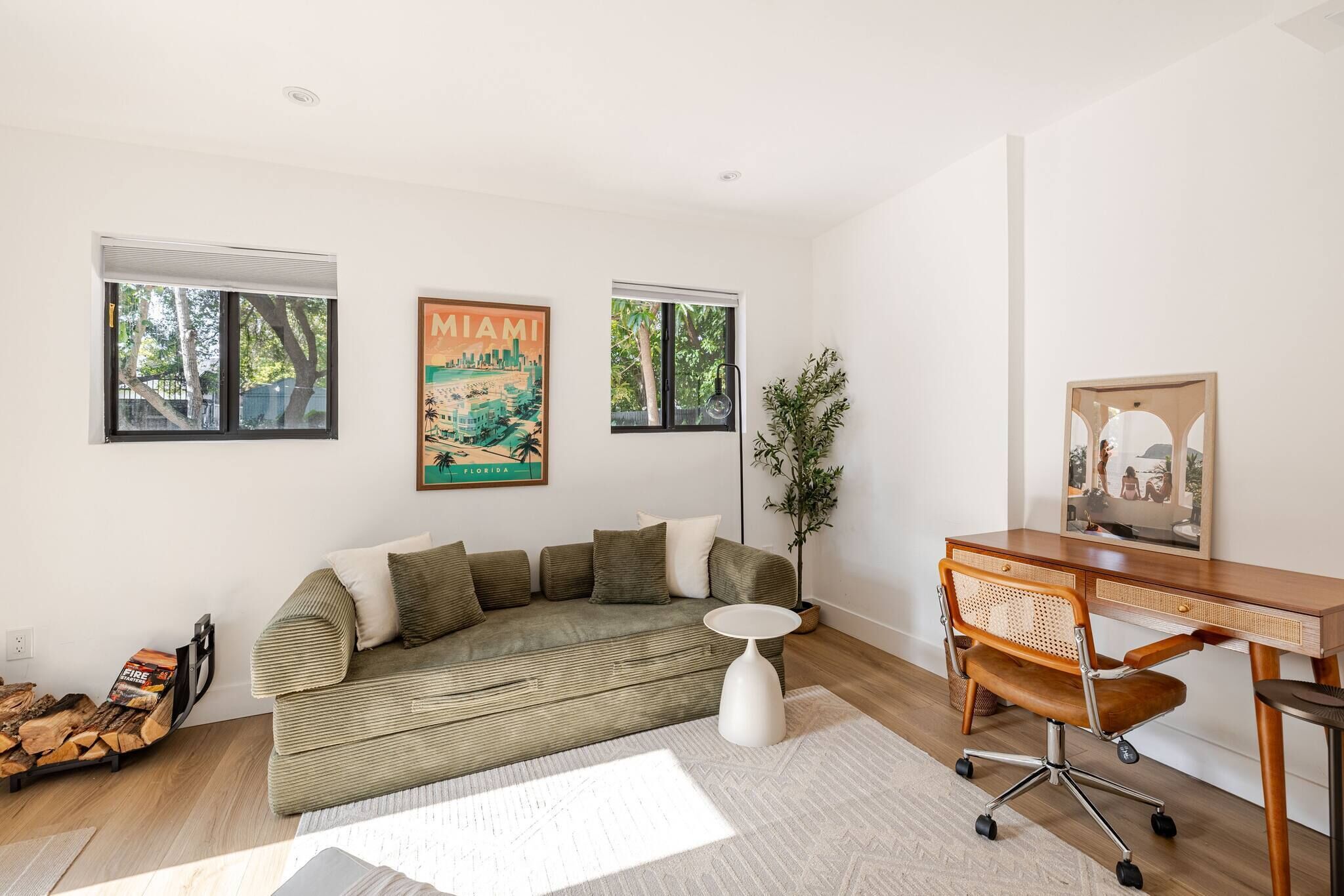 Un salon moderne avec un canapé vert, une petite table d’appoint blanche, un bureau en bois avec une chaise et un tableau encadré représentant Miami.