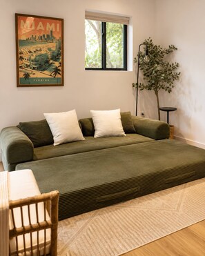 Una habitació amb llit, finestra, planta i un cartell a la paret.