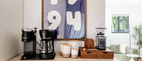 Una kitchenette con cafetera, licuadora y recipientes de almacenamiento sobre una encimera de madera.