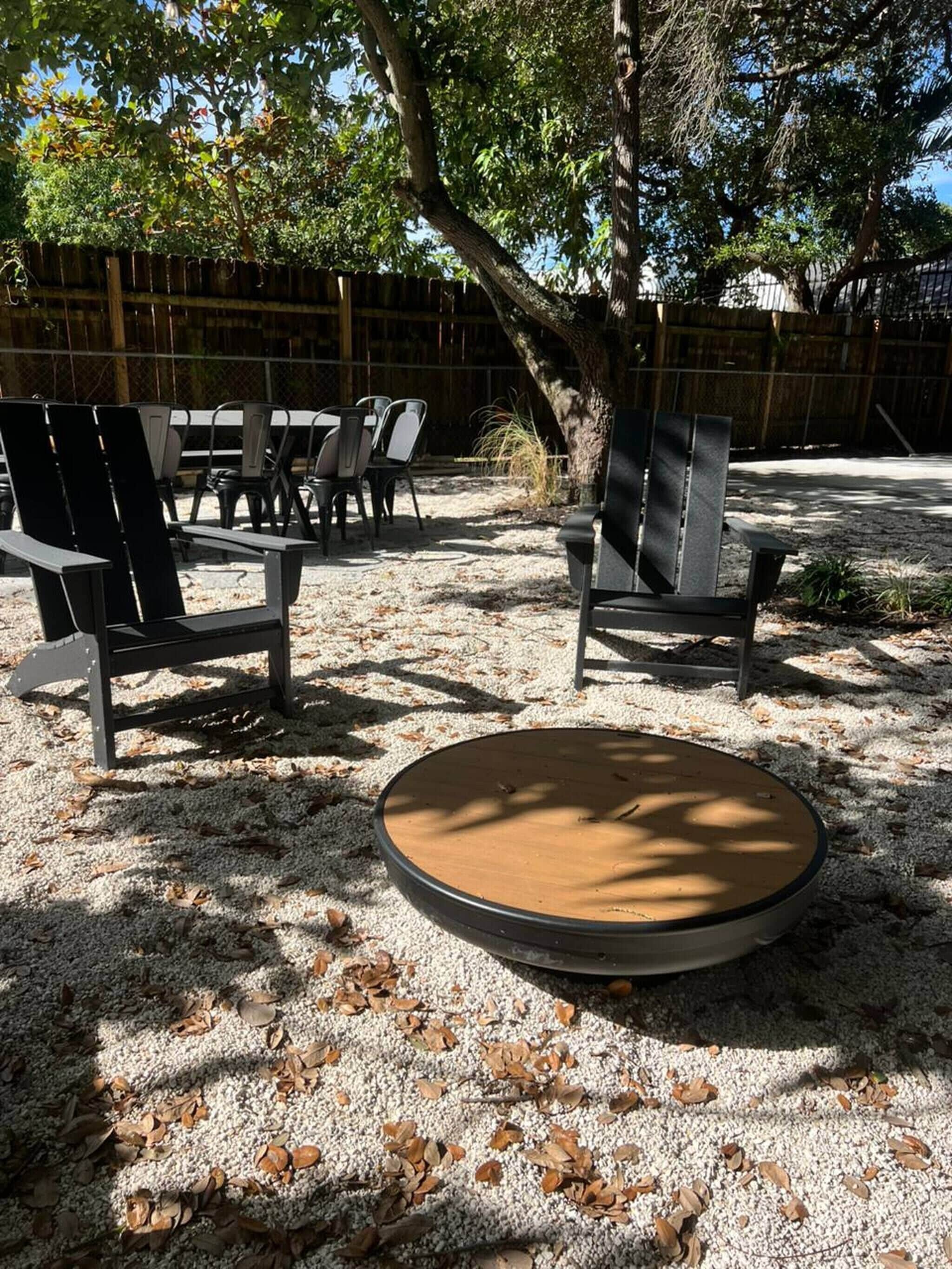 An outdoor seating area with chairs and a round table, surrounded by trees and a wooden fence.